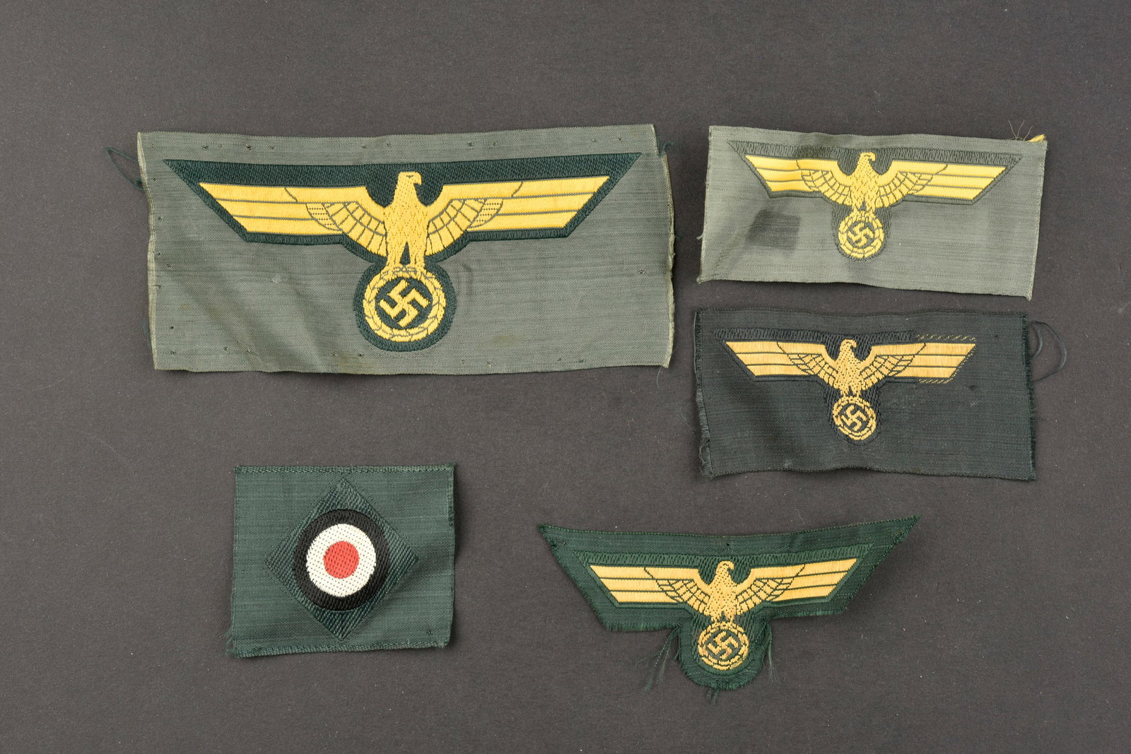 Insignes artillerie cotiere. Coastal artillery badges.: Insignes de l artillerie cotiere. Comprenant un aigle de poitrine Bevo, jamais monte. Trois modeles differents d aigles de coiffure Bevo, jamais montes. Une cocarde Bevo, jamais montee. Traces de coll