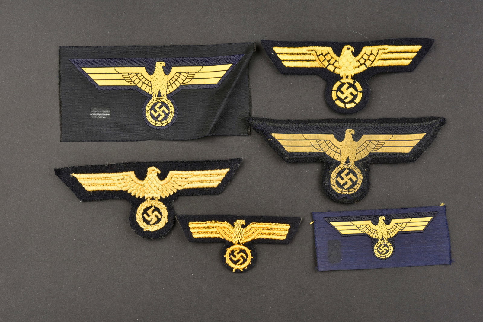 Insignes KM. Kriegsmarine insignia.: Insignes de la Kriegsmarine. Comprenant un aigle de poitrine brode sur drap bleu marine. Un aigle de poitrine Bevo, jamais monte, traces de colle au dos. Un aigle de coiffure brode sur support en drap