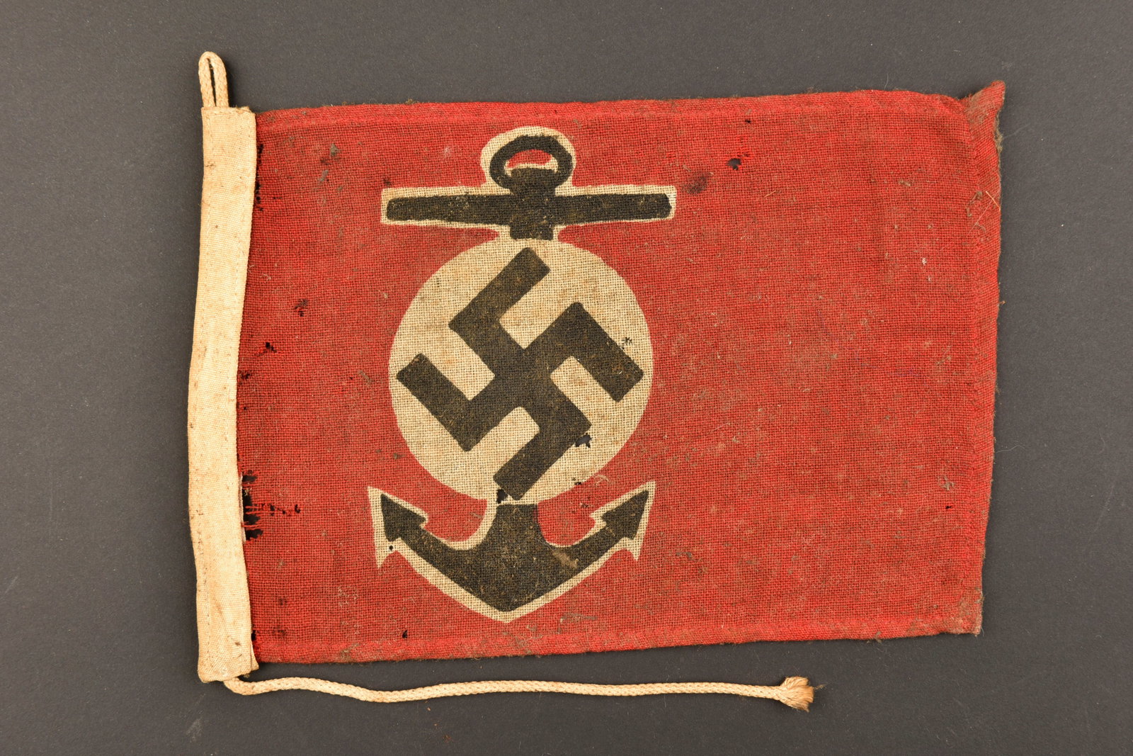 Marque Maritime Kriegsmarine. Maritime Kriegsmarine mark.: Marque Maritime Kriegsmarine. En tissu coton rouge. Insigne representant une ancre de marine et l’insigne national imprime. Biface. Les cordons de fixation au mat sont presents. Sans marquages visib