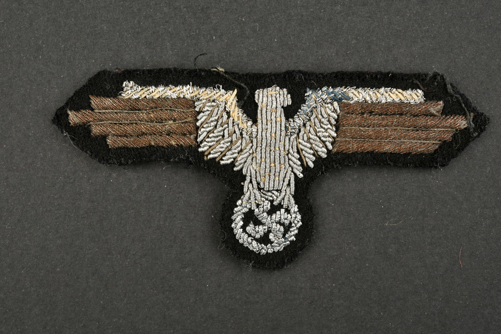 Aigle de manche SS. SS sleeve eagle.: Aigle de manche SS. Modele pour officier en cannetille argent sur fond en drap noir. Dos de la piece double en papier blanc. Modele de fabrication francaise. A noter une certaine usure et patine de la