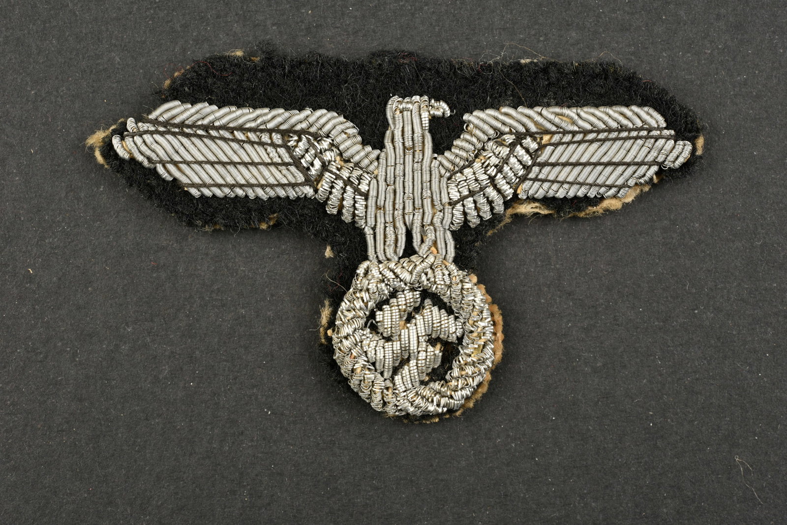 Aigle de coiffure SS. SS eagle cap.: Aigle de coiffure SS. Modele pour officier en cannetille argent sur fond en drap noir. Dos de la piece double en papier. Modele de fabrication francaise. A noter une certaine usure et patine de la pie