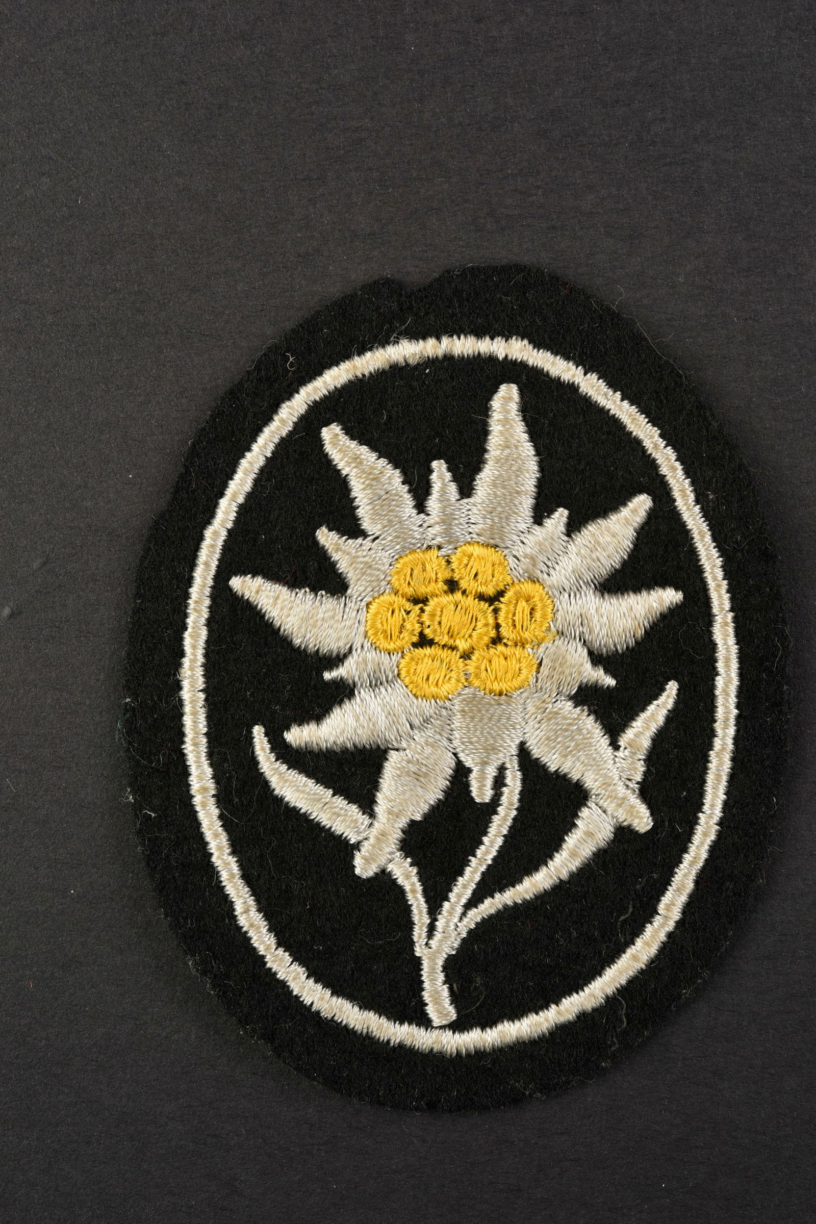 Edelweiss SS.: Edelweiss SS. Modele tisse sur fond noir. Jamais monte. Neuf de stock. A noter une certaine usure et patine de la piece. Etat II+. Edelweiss SS. Woven pattern on black background. Never mounted. New f