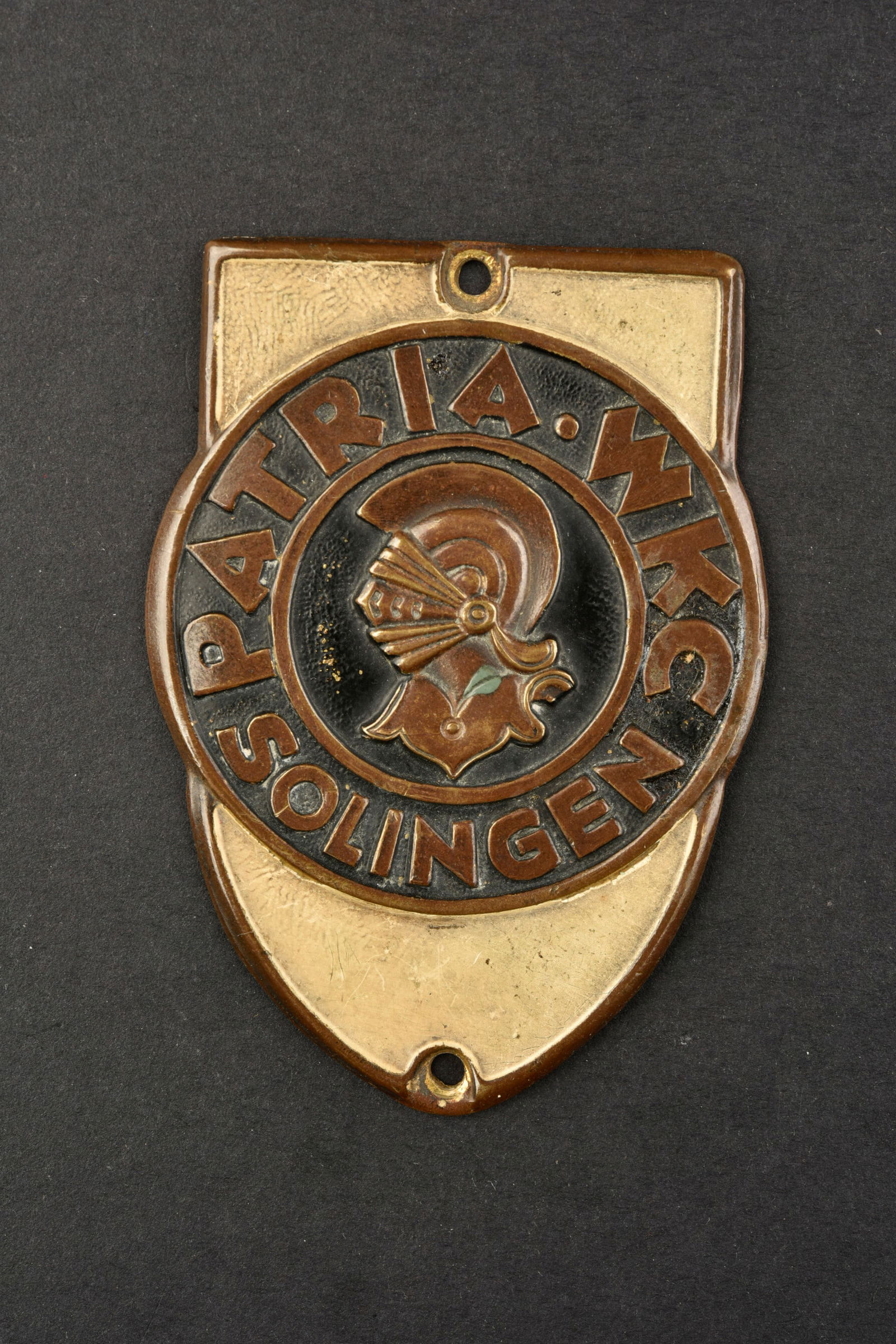Plaquette WKC. WKC brochure.: Plaquettes WKC. Plaquette en metal embouti peinte. Marquages Patria WKC Solingen. Deux points de fixation. Dimensions 4,8 x 6,8 cm. A noter une certaine usure et patine de la piece. Etat II+. WKC inse