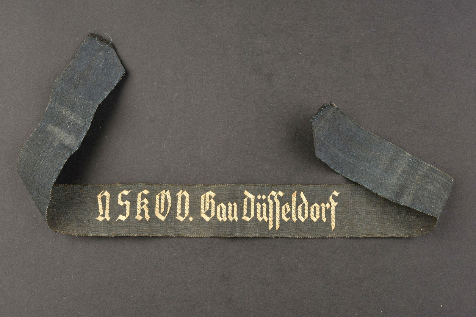 Bande de bras NSKOV. NSKOV arm band.: Bande de bras NSKOV. En tissu noir, broderie blanche. Marquages NSKOV Gau Dusseldorf. Longueur 37 cm. A noter une certaine usure et patine de la piece, ainsi que des ta ches. Etat II+. NSKOV arm band.