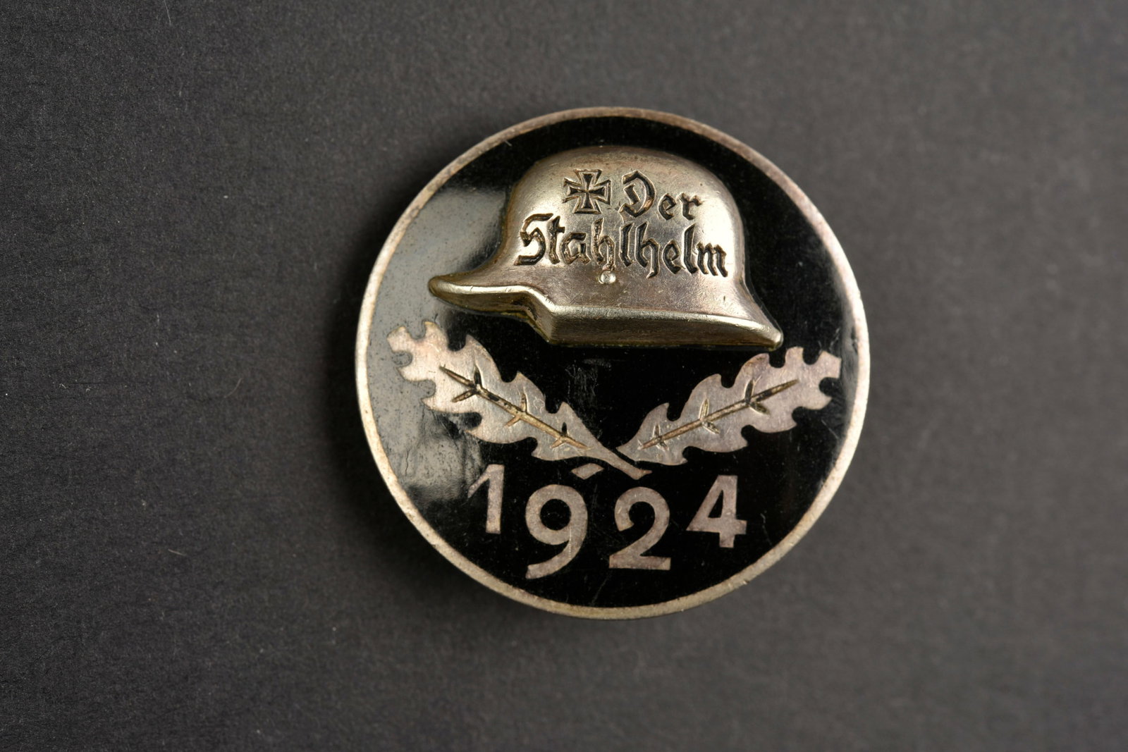 Insigne Der Stahlhelm. Der Stahlhelm insignia.: Insigne der Stahlhelm. En metal emaille noir, casque en relief, marquages Der Stahlhelm 1924. Fabrication STH Ges Gesch. Attache complete. Gravure manuscrite V HE 83 1924. A noter une certaine usure e