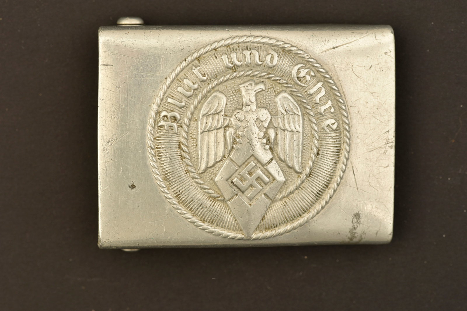 Boucle de ceinturon HJ. HJ Belt buckle.: Boucle de ceinturon Hitlerjugend. En aluminium, couleur argent. Boucle a deux ardillons presente. Marquages RZM M4/38, correspondant au fabricant Richard Sieper & Sohne Ludenscheid. A noter une certai