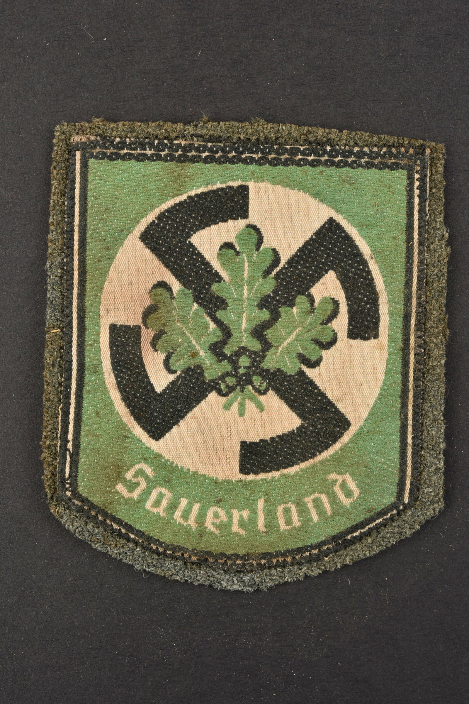 Insigne Sauerland. Sauerland insignia.: Insigne Sauerland. Modele tisse sur fond en drap Feldgrau, monte d'origine. A noter une certaine usure et patine de la piece, ainsi que des taches. Etat II+. Sauerland badge. Woven pattern on a Feldgr