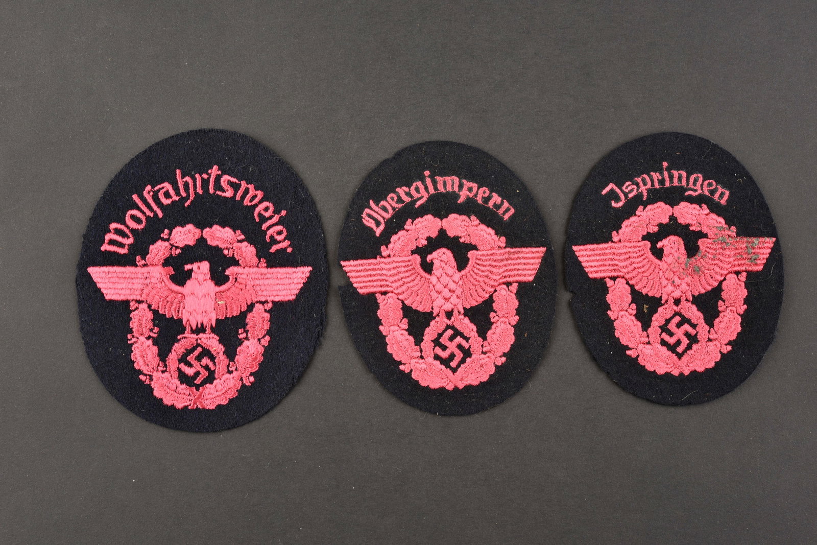 Insignes de manche de pompier. Fireman's sleeve badges.: Insignes de manche des pompiers du Reich. Comprenant un insigne en drap noir, broderie rose, marquee Obergimpern. Un insigne de manche en drap noir, broderie rose, marquee Ispringen. Un insigne de man