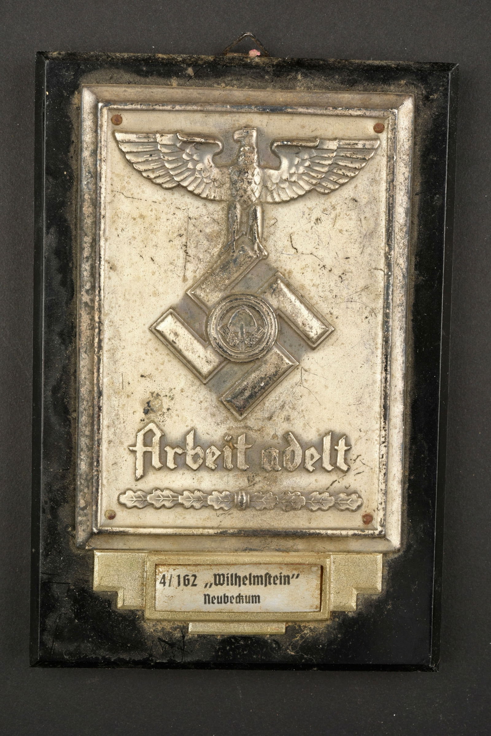 Plaquette du RAD. RAD insignia.: Plaquettes du RAD. Support en bakelite noire. Attache murale complete. Plaque en metal, aigle et mention Arbeit Adelt en relief. Petite plaque marquee 4/162 Wilhelmstein Neubeckum. Dimensions 10,5 x 1