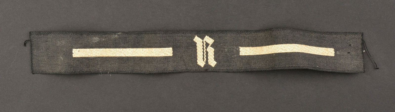 Bande de bras RAD. RAD cuff tittle.: Bande de bras RAD. EN tissu noir, avec lisere blanc. Lettre R tissee. Longueur 22 cm. A noter une certaine usure et patine de la piece, ainsi que quelques taches, visiblement incomplete. Etat II+. RAD