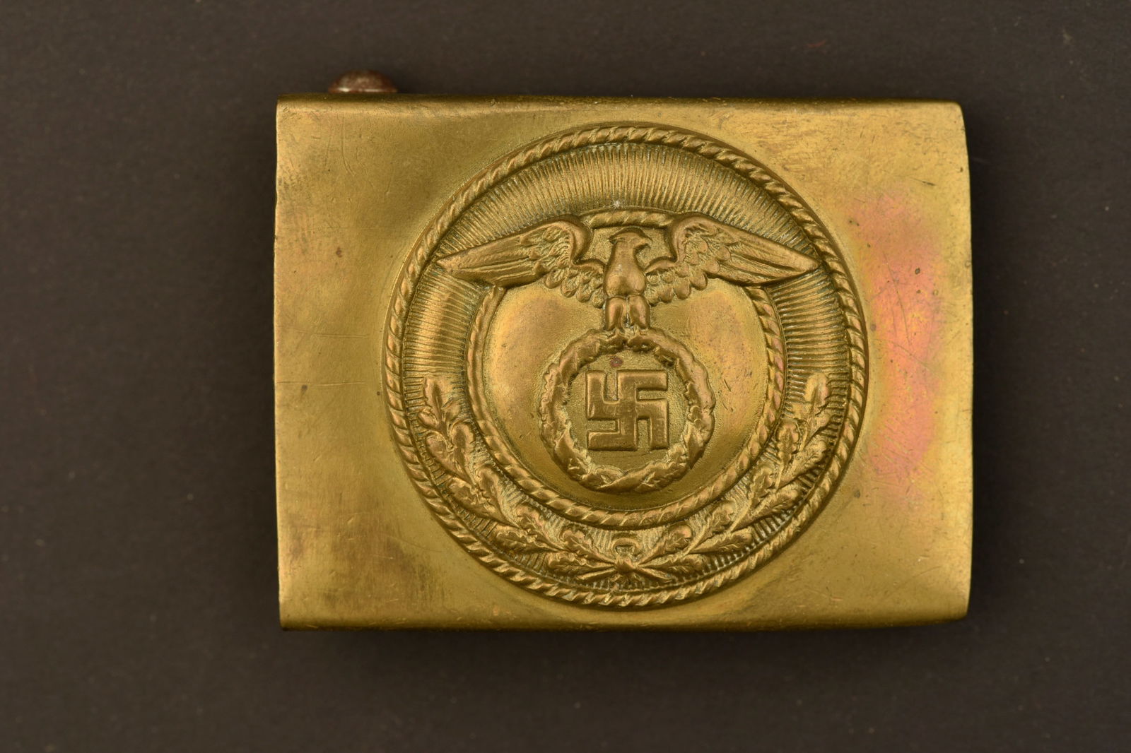 Boucle de ceinturon SA. SA belt buckle.: Boucle de ceinturon SA. En metal laiton. Insigne en relief. Boucle a deux ardillons presente. Sans marquages visibles. A noter une certaine usure et patine de la piece. Etat II+. SA belt buckle. Brass