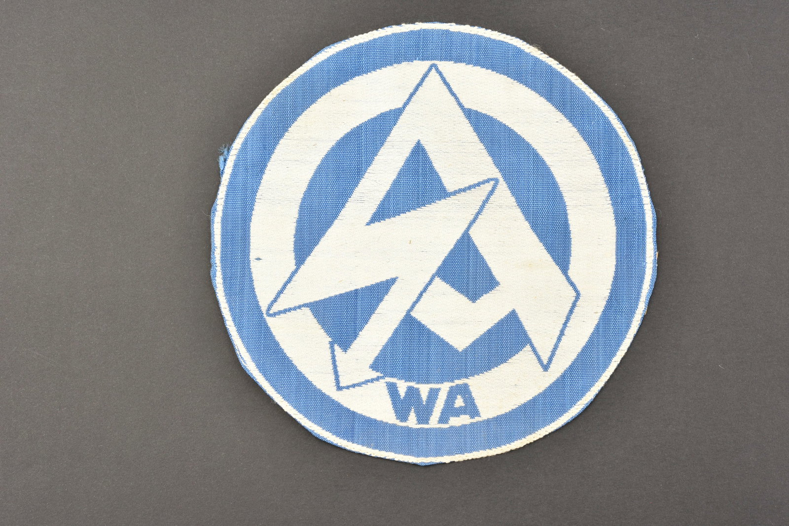 Insigne SA. SA insignia.: Insigne de maillot de sport SA. Modele tisse sur fond blanc, logo SA en tisse en fils bleu roi, lettrage WA. Jamais monte. Sans marquages visibles. Diametre 15 cm. Etiquette RZM numero 171964, code fa