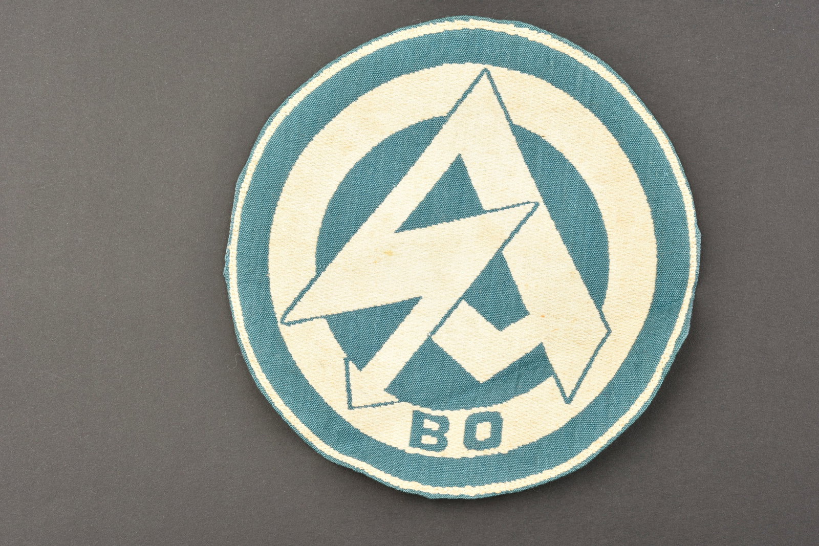 Insigne SA. SA insignia.: Insigne de maillot de sport SA. Modele tisse sur fond blanc, logo SA en tisse en fils bleu turquoise, lettrage BO. Jamais monte. Sans marquages visibles. Diametre 14,5 cm. Etiquette RZM absente. A not