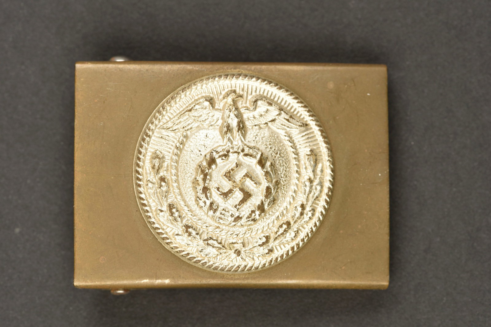 Boucle de ceinturon SA. SA belt buckle.: Boucle de ceinturon SA. Petit modele. En laiton. Insigne couleur argent. Fabrication en deux parties. Sans marquages visibles. Traces d'oxydation au dos. A noter une certaine usure et patine de la pie