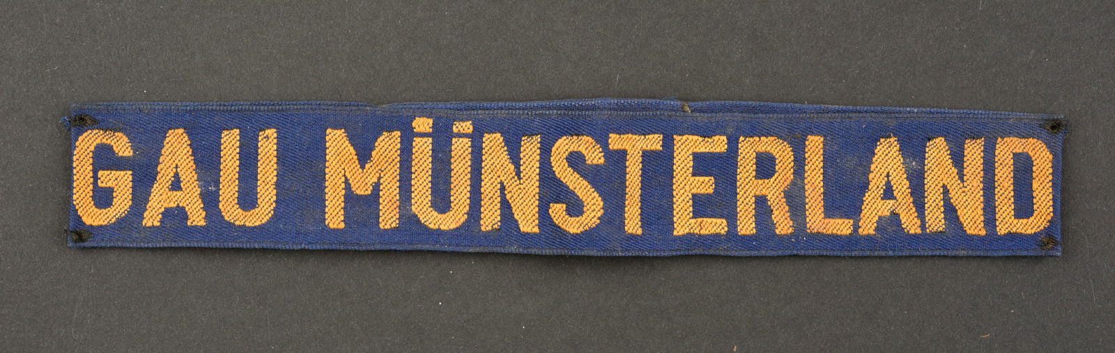 Bande de bras Gau Munsterland. Munsterland cuff tittle.: Bande de bras Gau Munsterland. En tissu bleu, cousue d'origine, marquages de couleur jaune Gau Munsterland. A noter une certaine usure et patine de la piece, ainsi que des accrocs et des taches. Etat