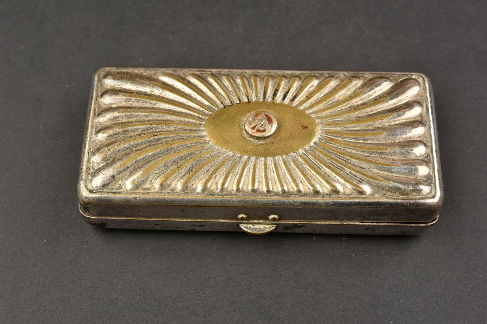 Boite SA. SA box.: Boite SA. En metal couleur argent. Couvercle tres bien decore. Insigne SA emaille present sur le couvercle. Dimensions 10,5 x 4,5x 2 cm. A noter une certaine usure et patine de la piece. Etat II+. SA