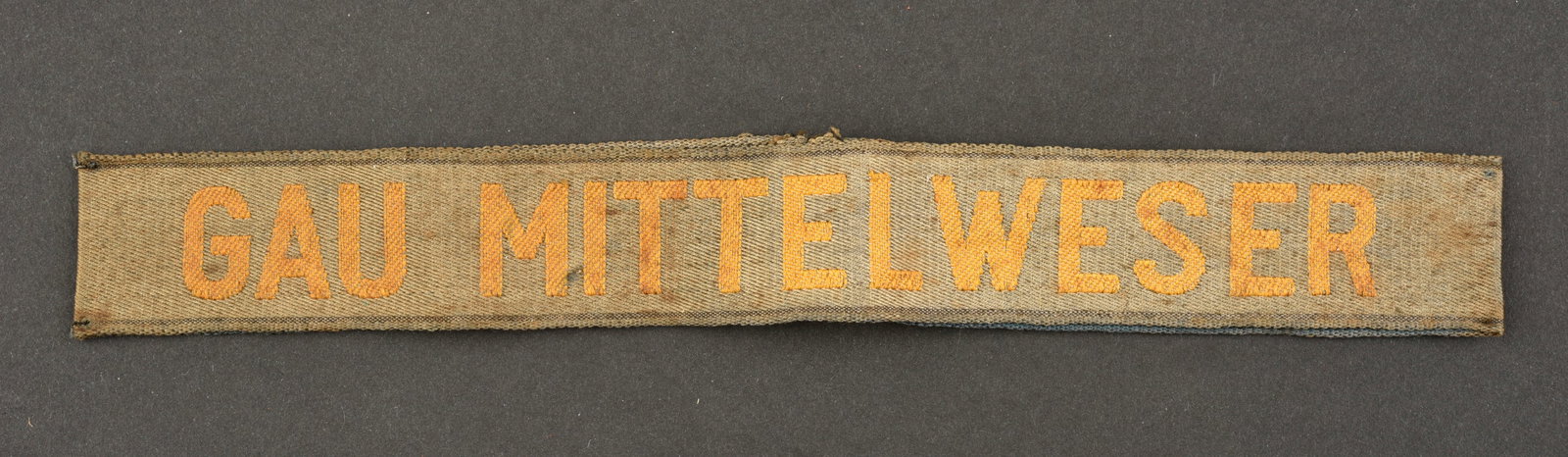 Bande de bras Gau Mittelweser. Gau Mittelweser cuff tittle.: Bande de bras Gau Mittelweser. En tissu bleu, cousue d'origine, marquages de couleur jaune Gau Mittelweser, fortement decoloree par le soleil. A noter une certaine usure et patine de la piece, ainsi q