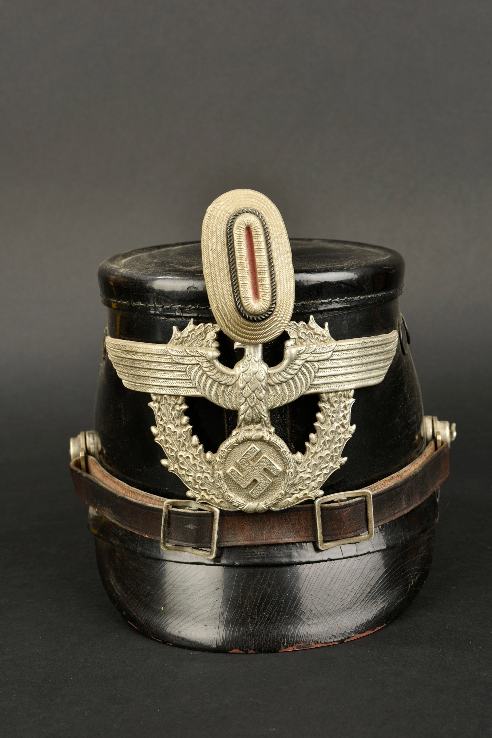 Shako Police. Police shako.: Shako Police. En fibre noire. Insigne et cocarde en aluminium. Les insignes n ont pas et e d emont es afin de v erifier les attaches. Jugulaire en cuir compl ete. Coiffe en cuir compl ete avec son cor