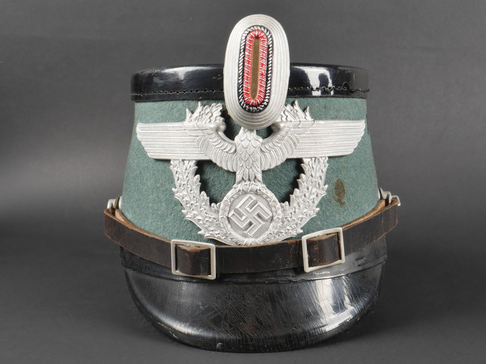 Shako Police. Police shako.: Shako Police. En fibre noire et drap Feldgrau. Insigne et cocarde en aluminium. Les insignes n ont pas et e d emont es afin de v erifier les attaches. Jugulaire en cuir compl ete. Coiffe en cuir compl