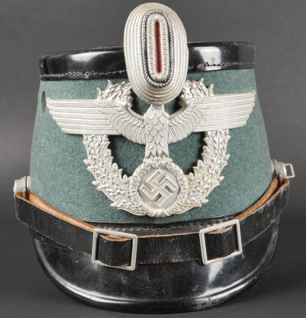Shako Police. Police shako.: Shako Police. En fibre noire et drap Feldgrau. Insigne et cocarde en aluminium. Les insignes n ont pas et e d emont es afin de v erifier les attaches. Jugulaire en cuir compl ete. Coiffe en cuir compl