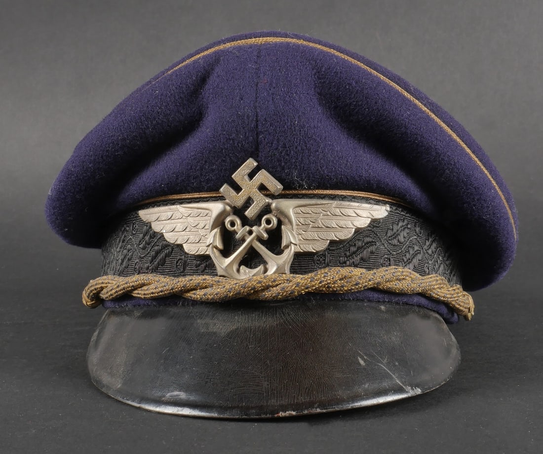 Casquette Luftwaffe. Lutfwaffe cap.: Casquette des services de recuperation des pilotes en mer. En drap bleu marine. Triple lisere or. Bandeau en mohair decore de feuilles de chene. Jugulaire tressee or et bleue. Insigne metallique des u