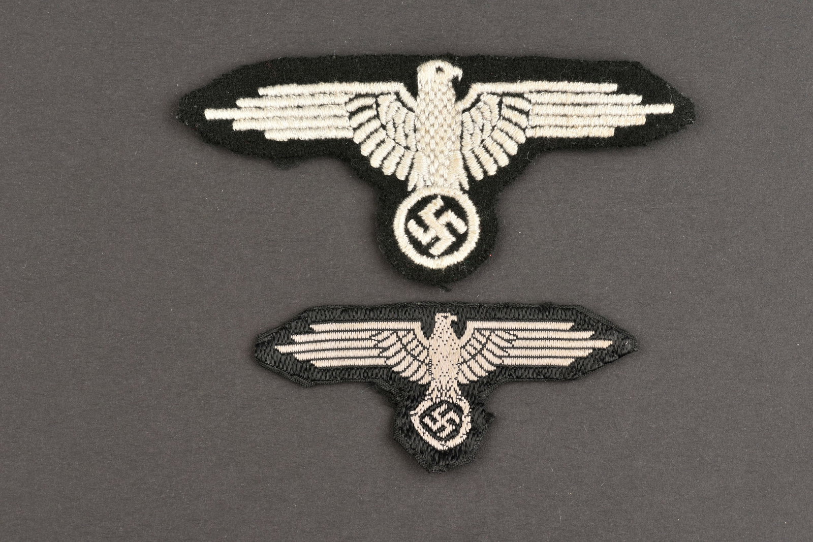 Aigles SS. SS eagles.: Aigles SS. Comprenant unaigle de manche en drap noir et broderie de couleur blanche celui-ci est une reproduction. Unaigle de coiffure Bevo, les bordures sont repliees de maniere reglementaire.a noter