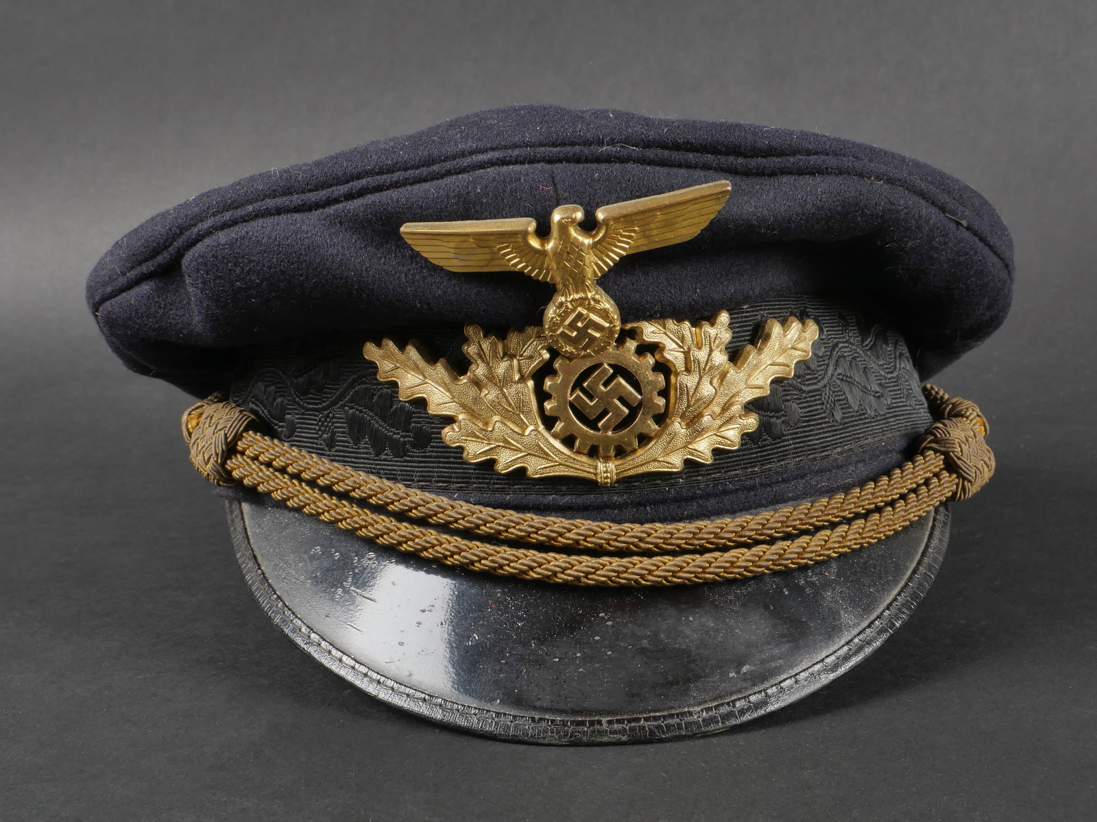 Casquette du DAF. German DAF cap.: Casquette du DAF. En tissu laineux bleu marine. Insignes en metal dore. Les insignes n ont pas ete demontesafin de verifier lesattaches. Fausse jugulaire doree. Bandeau de sudation en cuir fauve. Inte