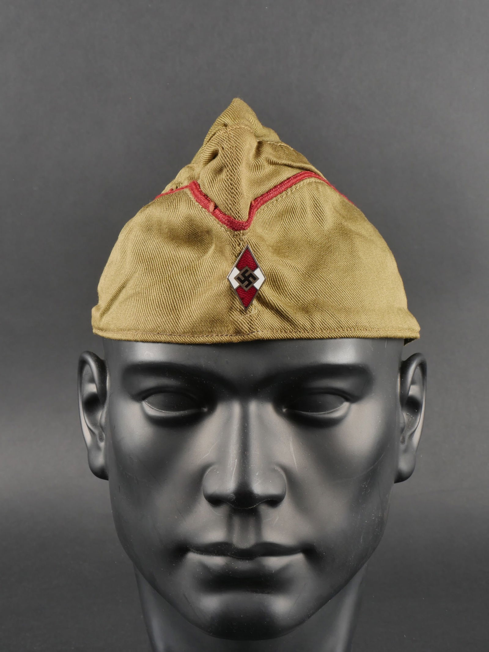 Calot Hitlerjugend. German Hitlerjugend cap.: Calot Hitlerjugend. En tissu soyeux beige. Lisere rouge fonce faisant le tour de la coiffure. Insigne metallique Hitlerjugend, sans marquages visibles. Interieur double en tissu vert. Trace d une etiq