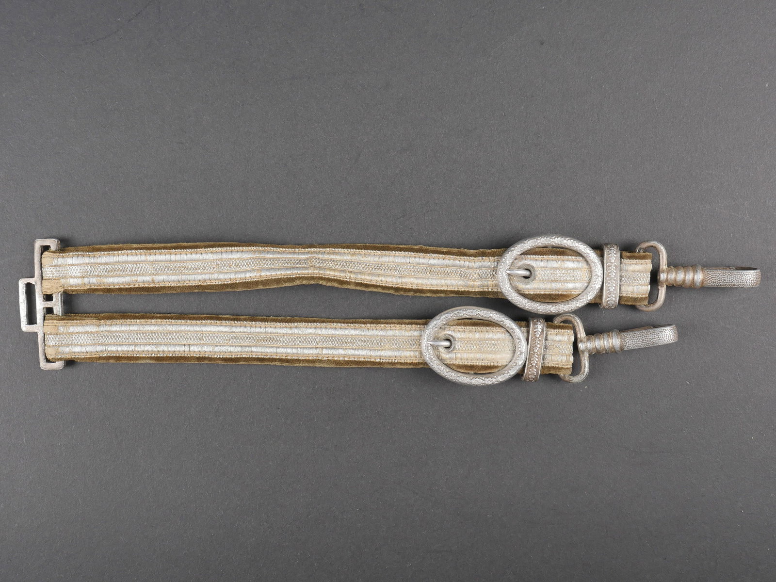 Belieres de dague Heer. Heer dagger hangers.: Belieres de dague Heer. Galons argent sur plateau en velours marron. Garnitures en metal, decorees de feuilles de chene. Les mousquetons sont fonctionnels. Attache complete. A noter une certaine usure