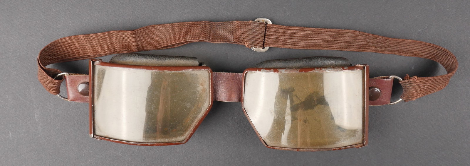 Lunette de motocycliste. Motorcyclist Goggles.: Lunette de motocycliste. Modele precoce. Armature en metal, couleur marron a 80%. Verres fumes. Doublure en caoutchouc noir et cuir marron. Elastique relativement souple. A noter une certaine usure et