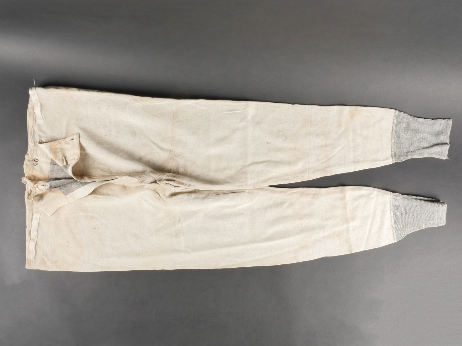 Calecon hivernal. German winter long underwear: Calecon hivernal. En tissu coton blanc, double d un drap de couleur gris. Feutrines au bas des jambes. Le cordon de serrage arriere est present, mais effiloche. Tous les boutons sont presents. Taille