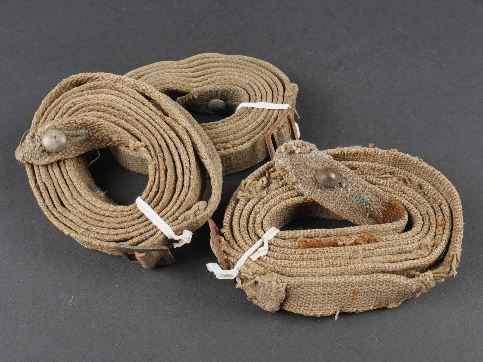 Sangles de masque anti-gaz. German gas mask straps.: Sangles de masque anti-gaz. Trois grandes sangles en forte toile Feldgrau, les tetons metalliques sont presents. A noter une certaine usure et patine des pieces. Etat II+. Gas mask straps. Three large