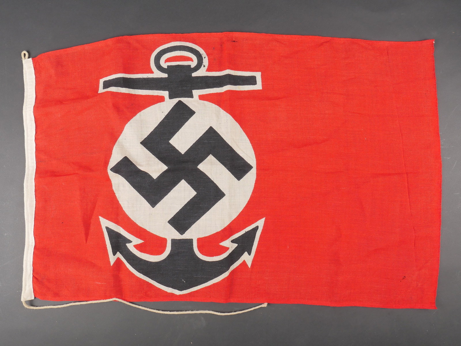 Marque Maritime Kriegsmarine. Kriegsmarine flag.: Marque Maritime Kriegsmarine. En tissu coton rouge. Insigne representant une ancre de marine et l’insigne national imprime. Biface. Les cordons de fixation au mat sont presents. Sans marquages visib