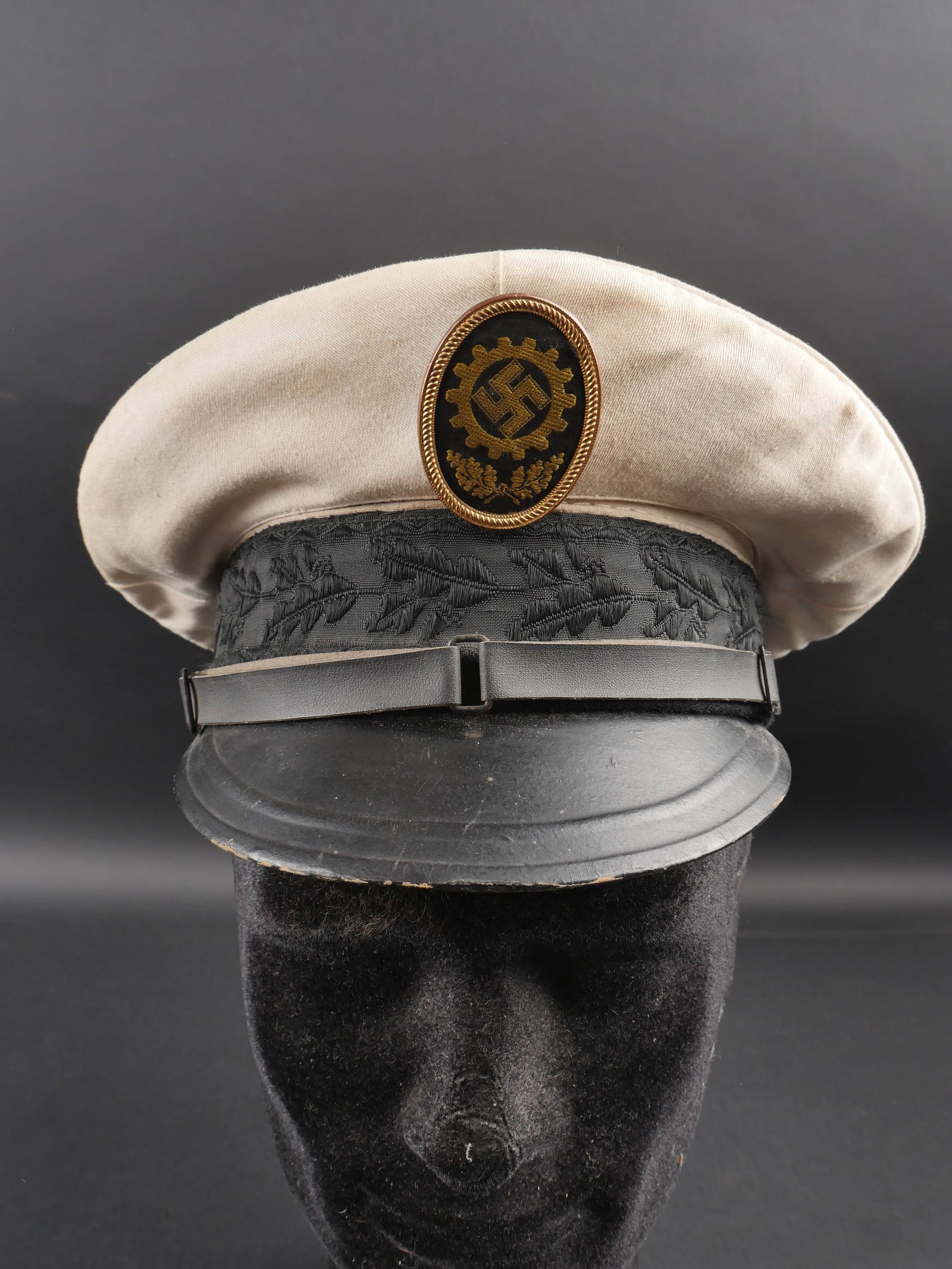 Caquette du DAF. German DAF cap.: Casquette du DAF. Coiffe blanche. Bandeau decore de feuilles de chene. Insigne tisse borde de metal. L insigne n a pas ete demonte afin de verifier les attaches. Fausse jugulaire complete. Interieur d