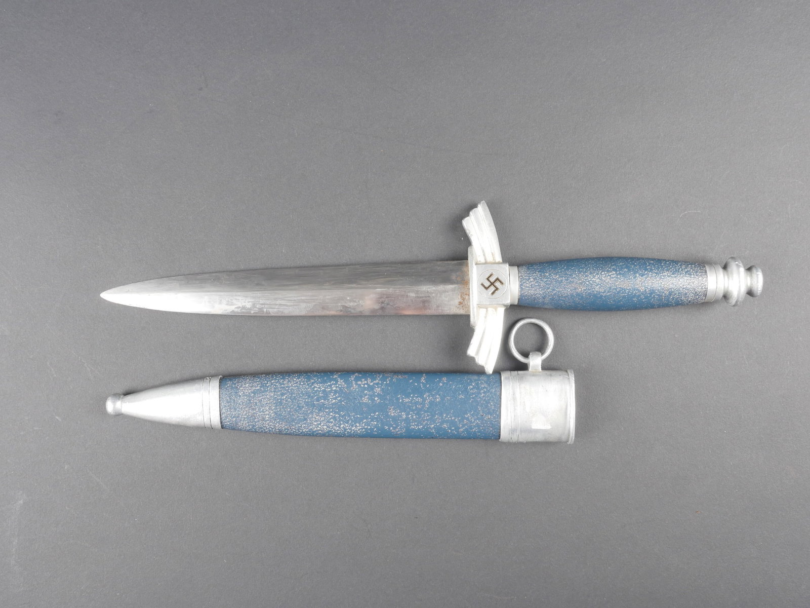 Dague DLV. German DLV dagger.: Dague du DLV. Garniture en metal. Un insigne national de la garde a perdu sa couleur. Poignee peinte en bleue. Belle lame presentant des marques d usure, pointe tres arrondie. Sans marquages visibles.