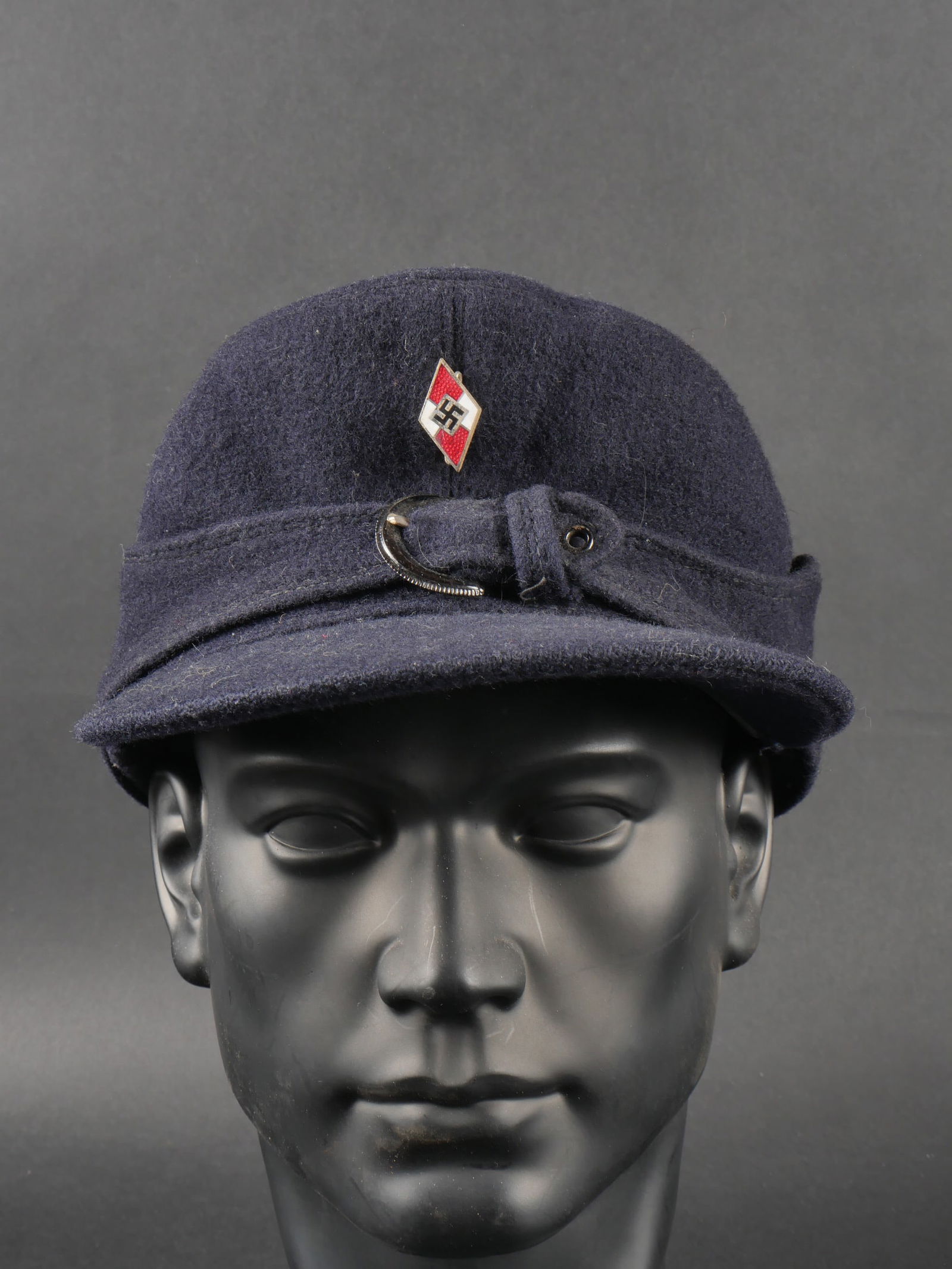 Casquette HJ. Hitlerjugend cap.: Casquette Hitlerjugend. En epais drap bleu marine. Rabat maintenu par une boucle a un seul ardillon. Probable fabrication civile. Insigne Hitlerjugend en metal emaille presentant quelques manques. L i
