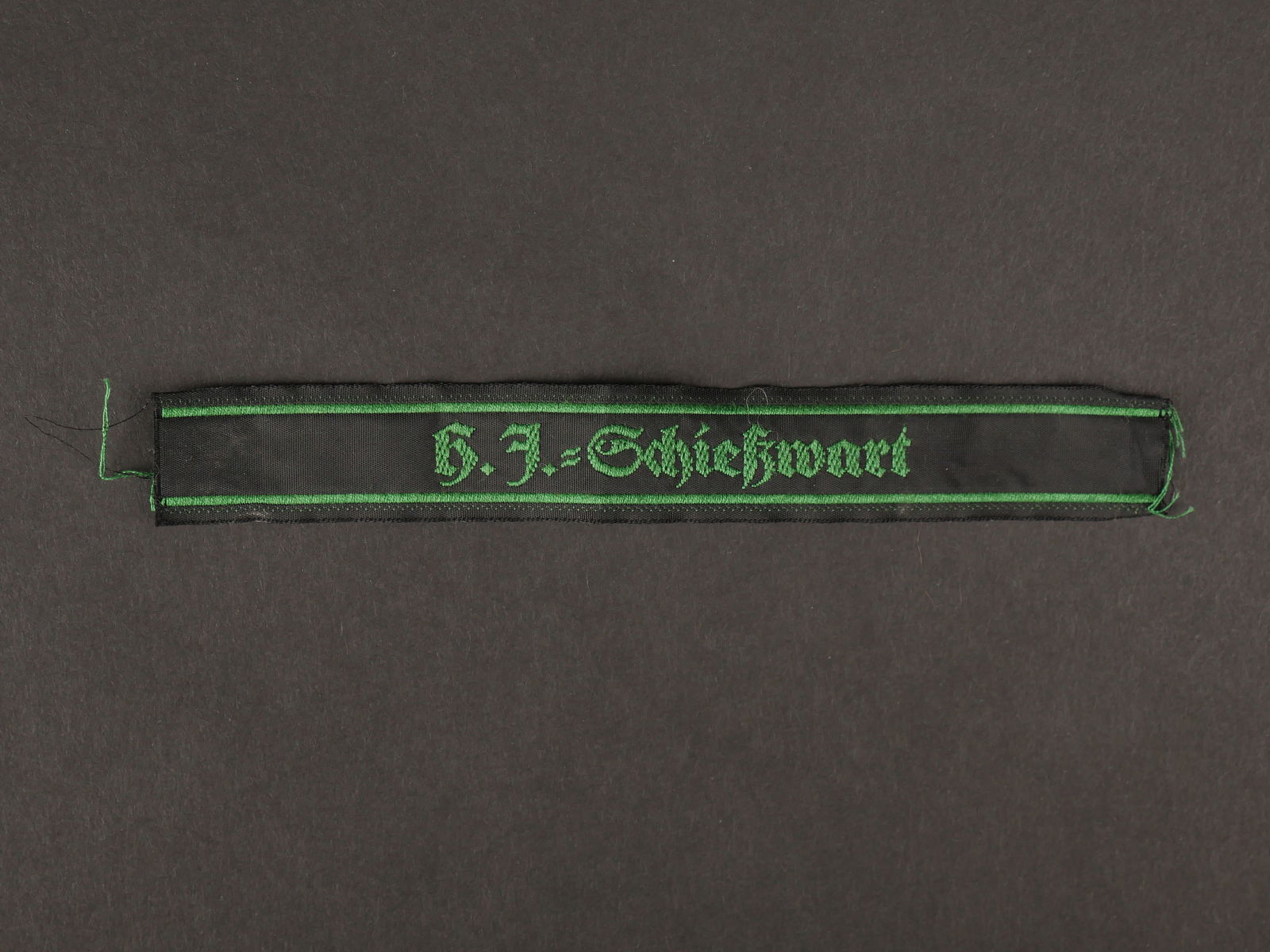 HJ Schiesswart.: Hitlerjugend Schiesswart. En tissu noir, tissage en fil vert, marque HJ Schiesswart. Longueur 14 cm. Jamais monte. A noter une legere usure et patine de la piece. Etat I-. Hitlerjugend Schiesswart. In