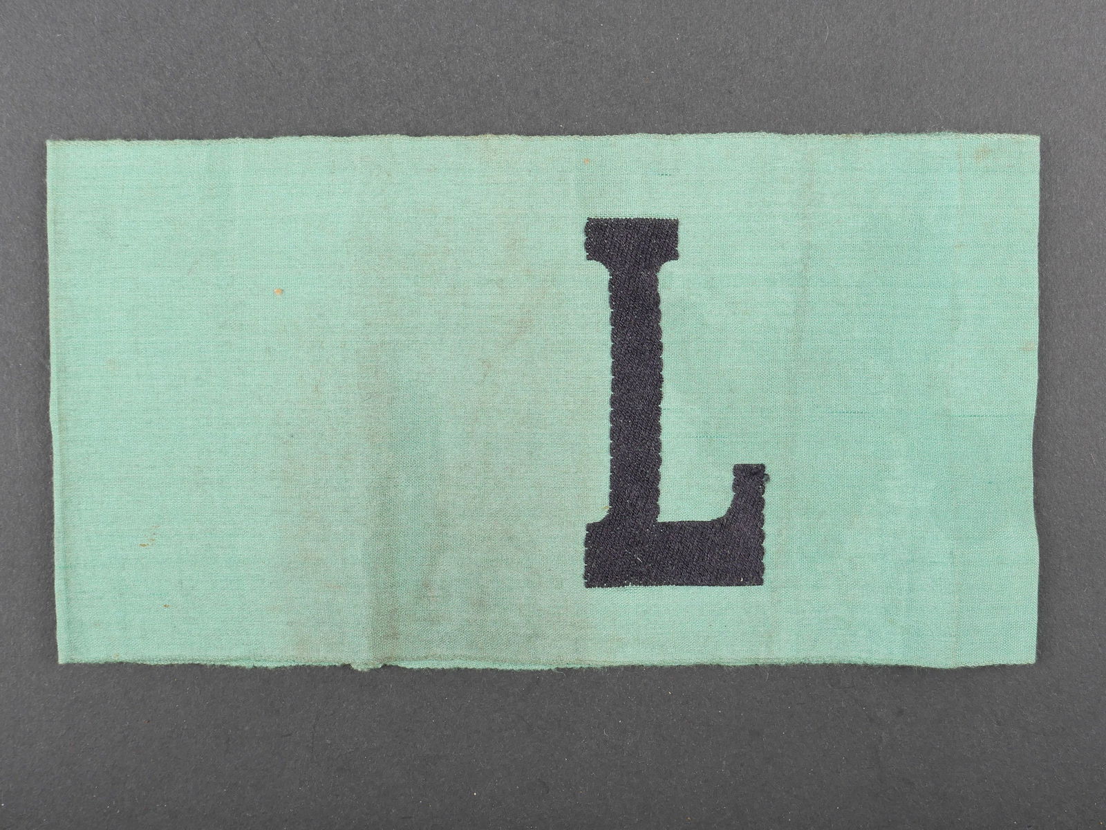 Brassard Luftschutz. Luftschutz armband.: Brassard Luftschutz. En tissu coton vert. Lettre L brode en fils noir. Sans marquages visibles. Modele pour les auxiliaires de la Luftschutz. A noter une certaine usure et patine de la piece, ainsi qu
