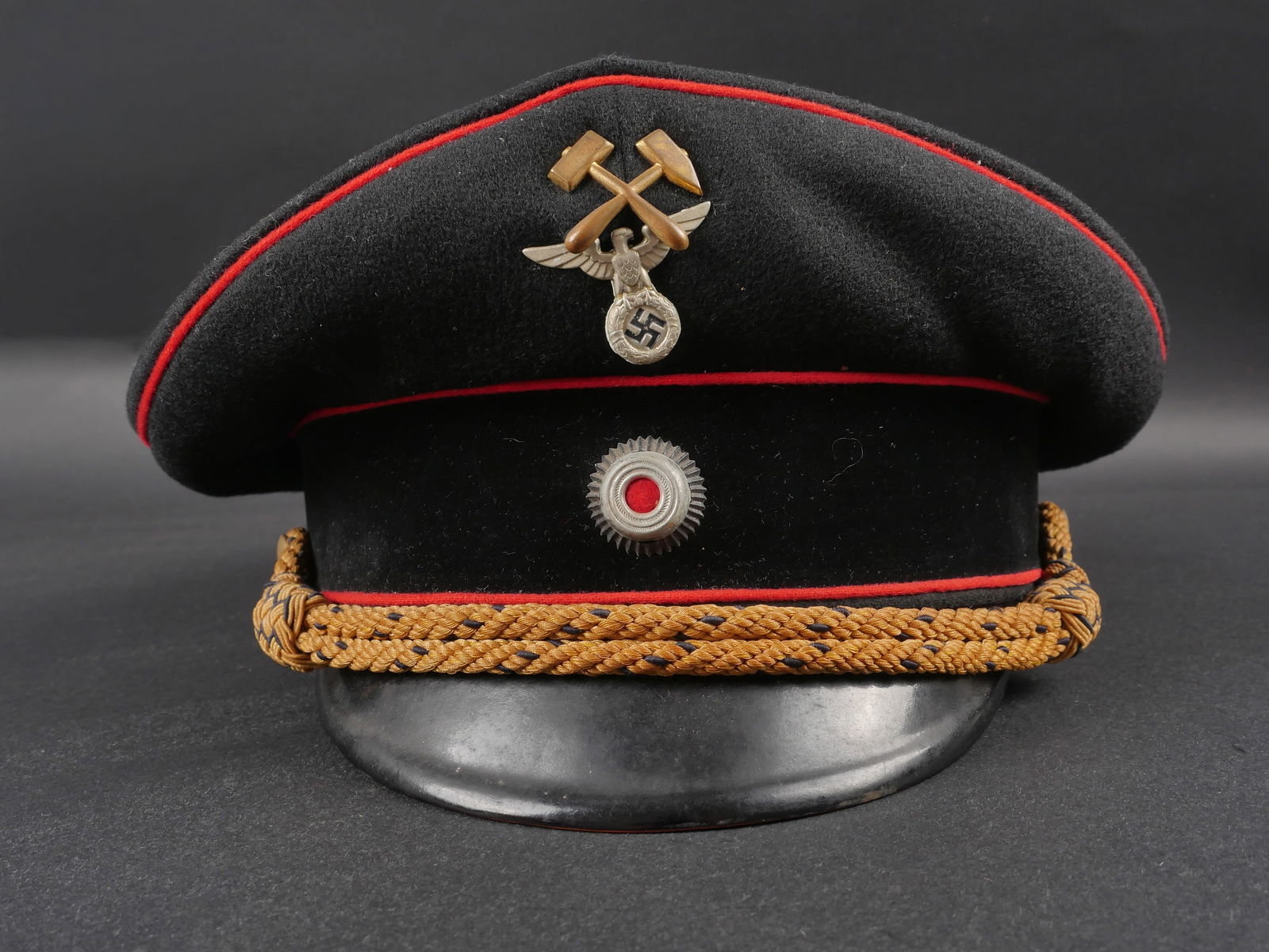 Casquette de mineur du Reich. Reich Miner’s Cap.: Casquette de mineur du Reich. En drap noir. Triple lisere rouge. Bandeau en velours noir. Insignes metalliques des mineurs du Reich. Les insignes n ont pas ete demontes afin de verifier les attaches.