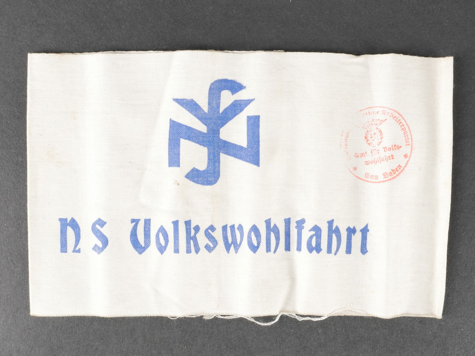 Brassard NSV. NSV armband.: Brassard NSV. En tissu coton blanc. Marquages imprimes en bleu NS Volkswohlfahrt. Tampon partiellement illisible mais marque Gau Baden. Les bordures sont partiellement effilochees. A noter une certain