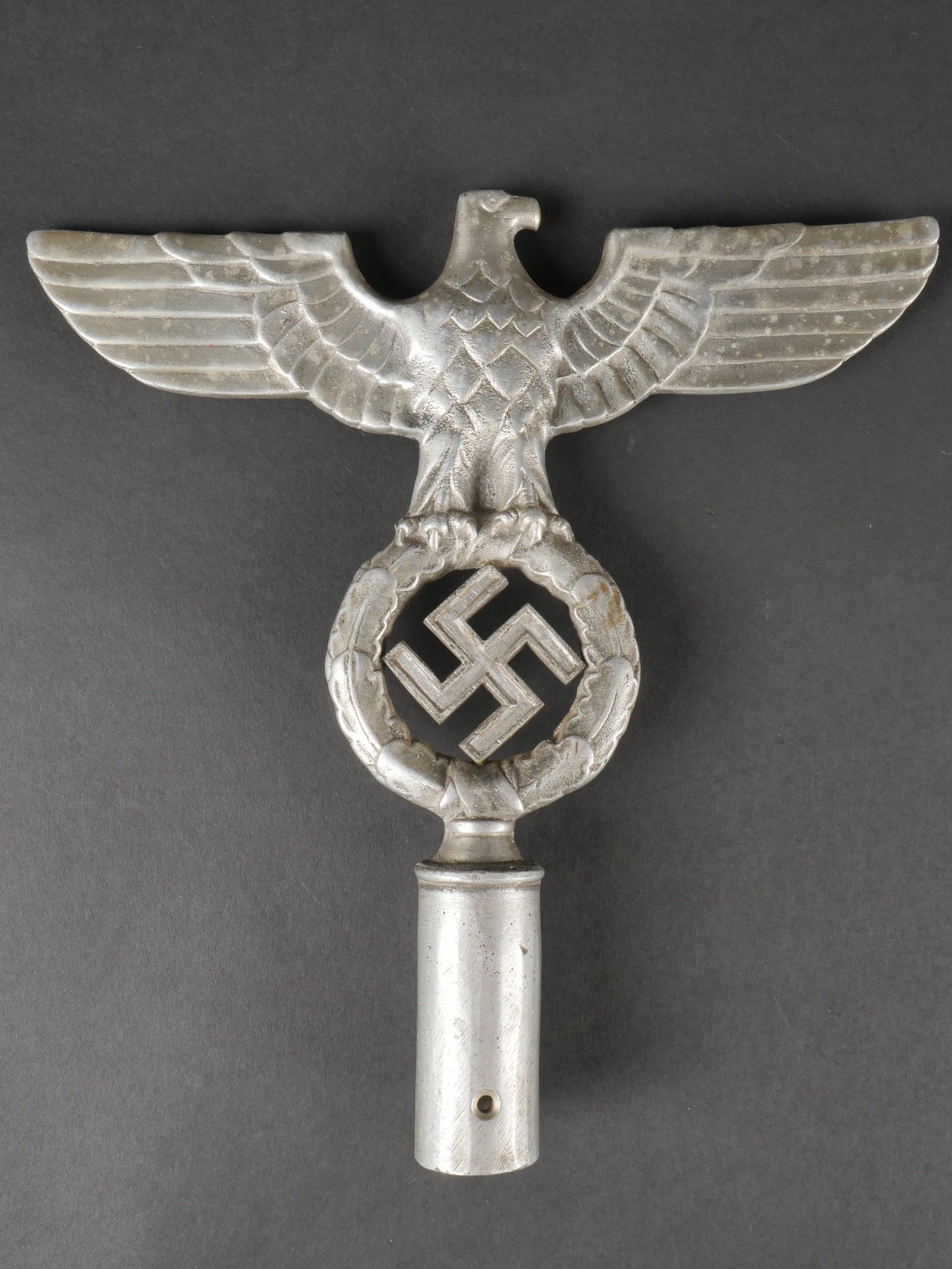 Pointe de drapeau. Flag tip.: Pointe de drapeau. En metal moule. Representant un aigle aux ailes deployees. Couleur argent a 60%. Sans marquages visibles. Hauteur 25 cm. Largeur 24 cm. A noter une certaine usure et patine de la pi