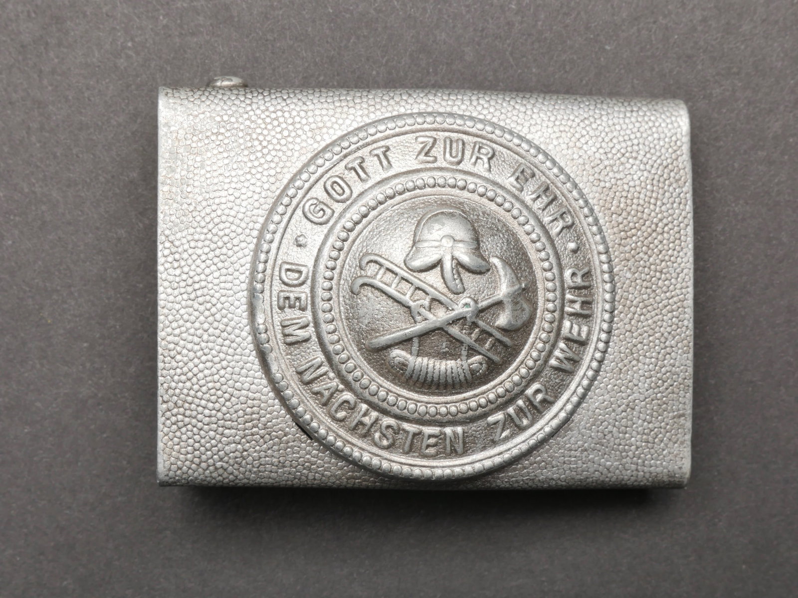Boucle de ceinturon Feuerschutzpolizei. Feuerschutzpolizei belt buckle.: Boucle de ceinturon Feuerschutzpolizei. En aluminium grenele couleur argent. Fabrication en deux parties. Marquages Gott Zur Ehr Dem Nachsten zur Wehr. Boucle a deux ardillons complete. Sans marquages