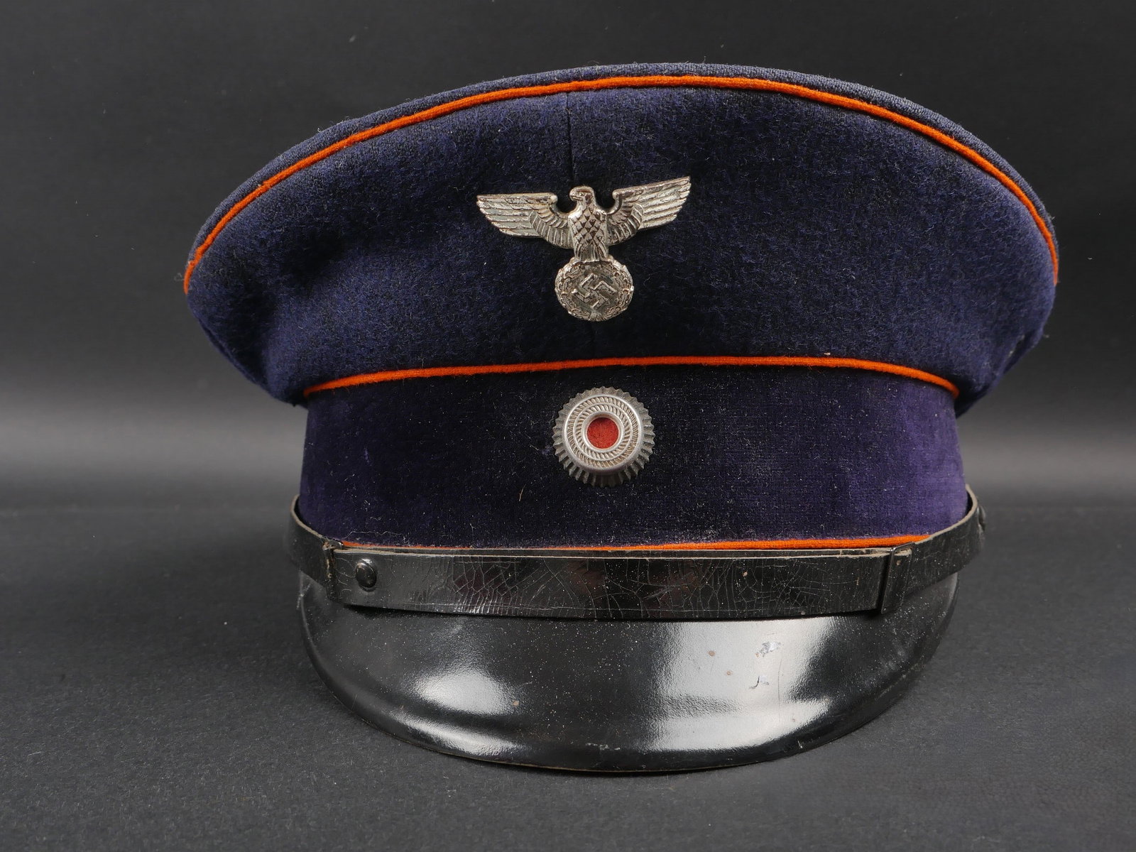Casquette des postes du Reich. Reich Post Cap: Casquette des postes du Reich. En drap bleu marine. Triple lisere orange. Bandeau en velours noir. Insignes metalliques. Les insignes n ont pas ete demontes afin de verifier les attaches. Fausse jugul