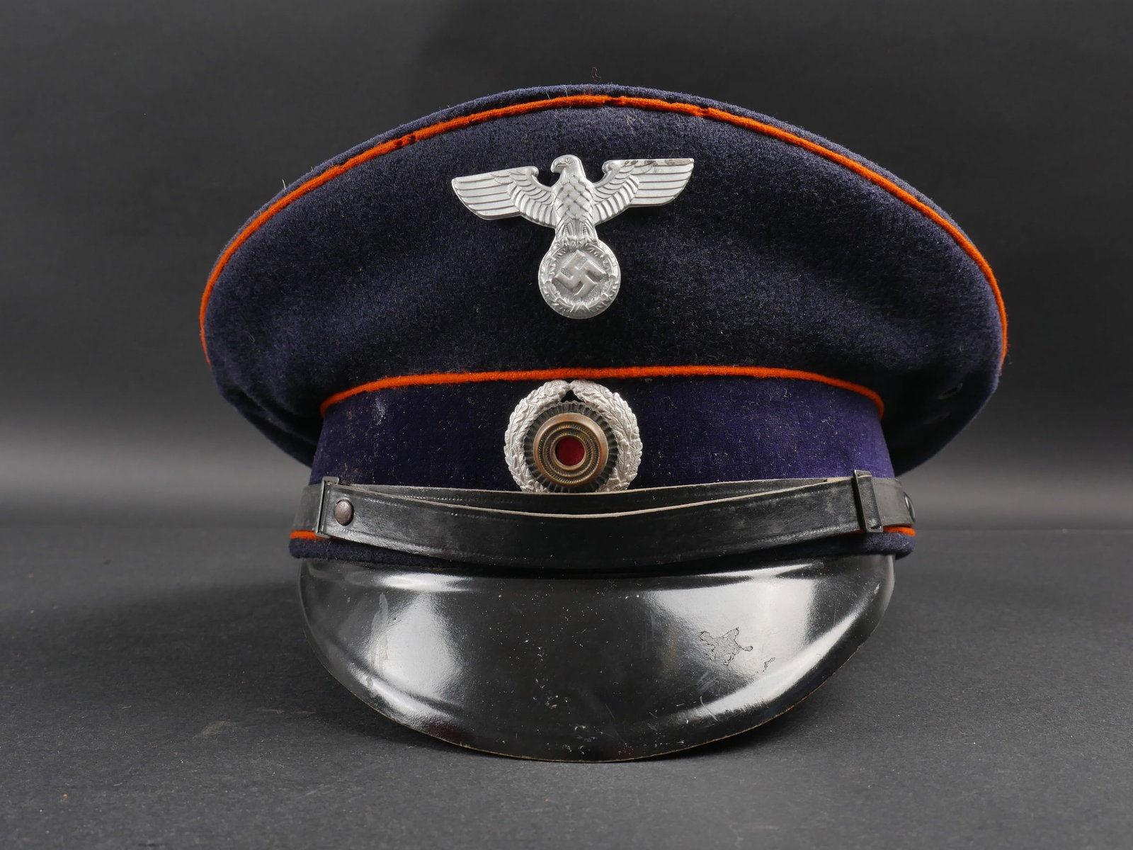 Casquette des postes du Reich. Reich Post Cap: Casquette des postes du Reich. En drap bleu marine. Triple lisere orange. Bandeau en velours noir. Insignes metalliques. Les insignes n ont pas ete demontes afin de verifier les attaches. Fausse jugul