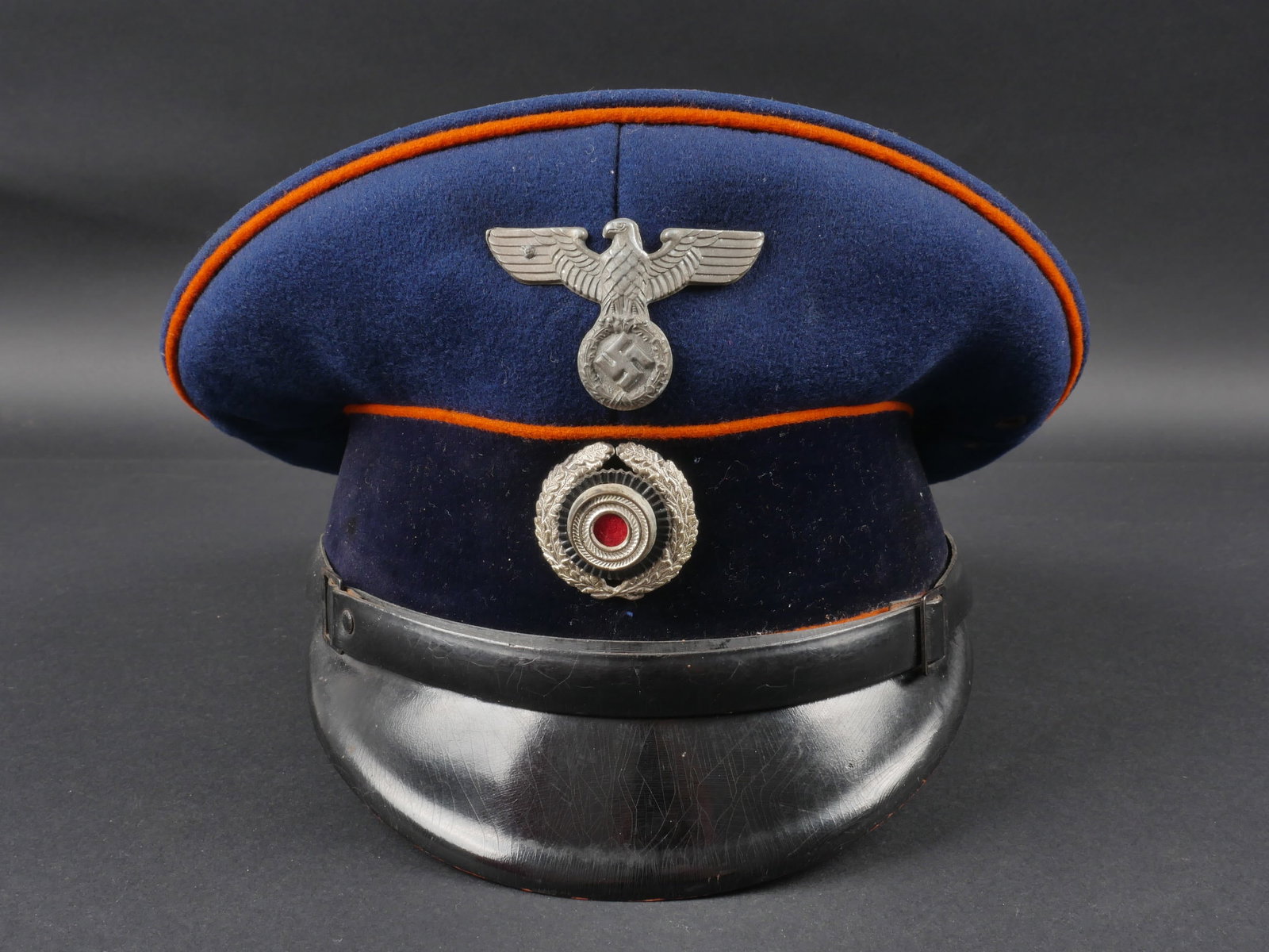Casquette des postes du Reich. Reich Post Cap: Casquette des postes du Reich. En drap bleu marine. Triple lisere orange. Bandeau en velours noir. Insignes metalliques. Les insignes n ont pas ete demontes afin de verifier les attaches. Fausse jugul