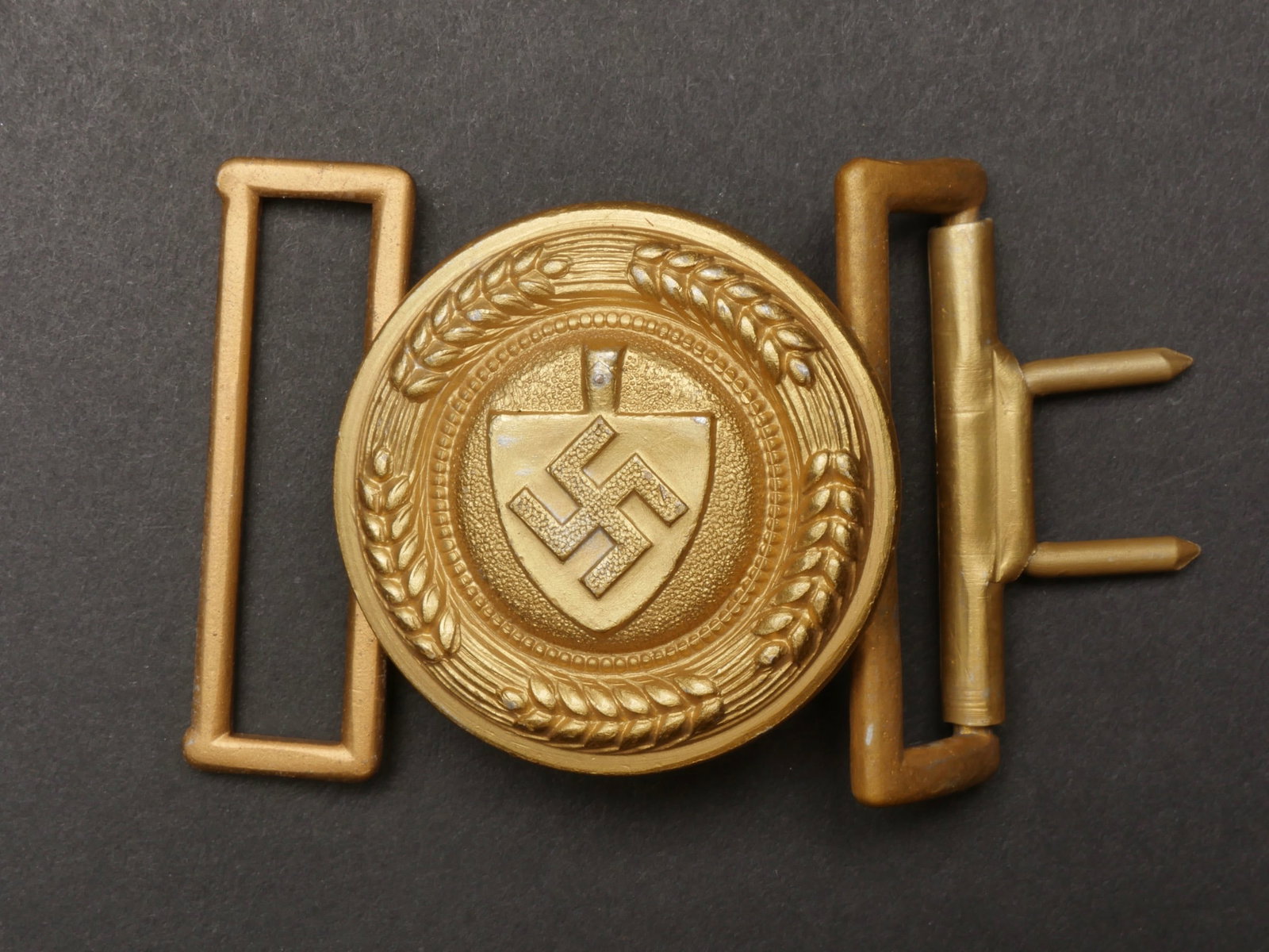 Boucle de ceinturon officier RAD. RAD officer belt buckle.: Boucle de ceinturon d officier RAD. En aluminium, dorure a 90%. Boucle a deux ardillons presente. Fabrication OLC Ges Gesch. A noter une certaine usure et patine de la piece. Etat II+. Belt buckle of 