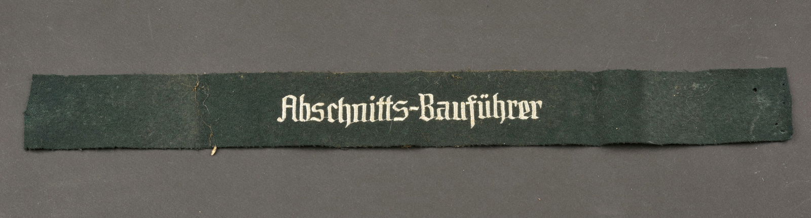 Bande de bras Abschnitts. Abschnitts cufftittle.: Bande de bras Abschnitts Baufuhrer. En drap vert fonce, broderie blanche. Largeur 5 cm. Longueur 48 cm. A noter une certaine usure et patine de la piece, ainsi que des trous de mite. Etat II+. Abschni