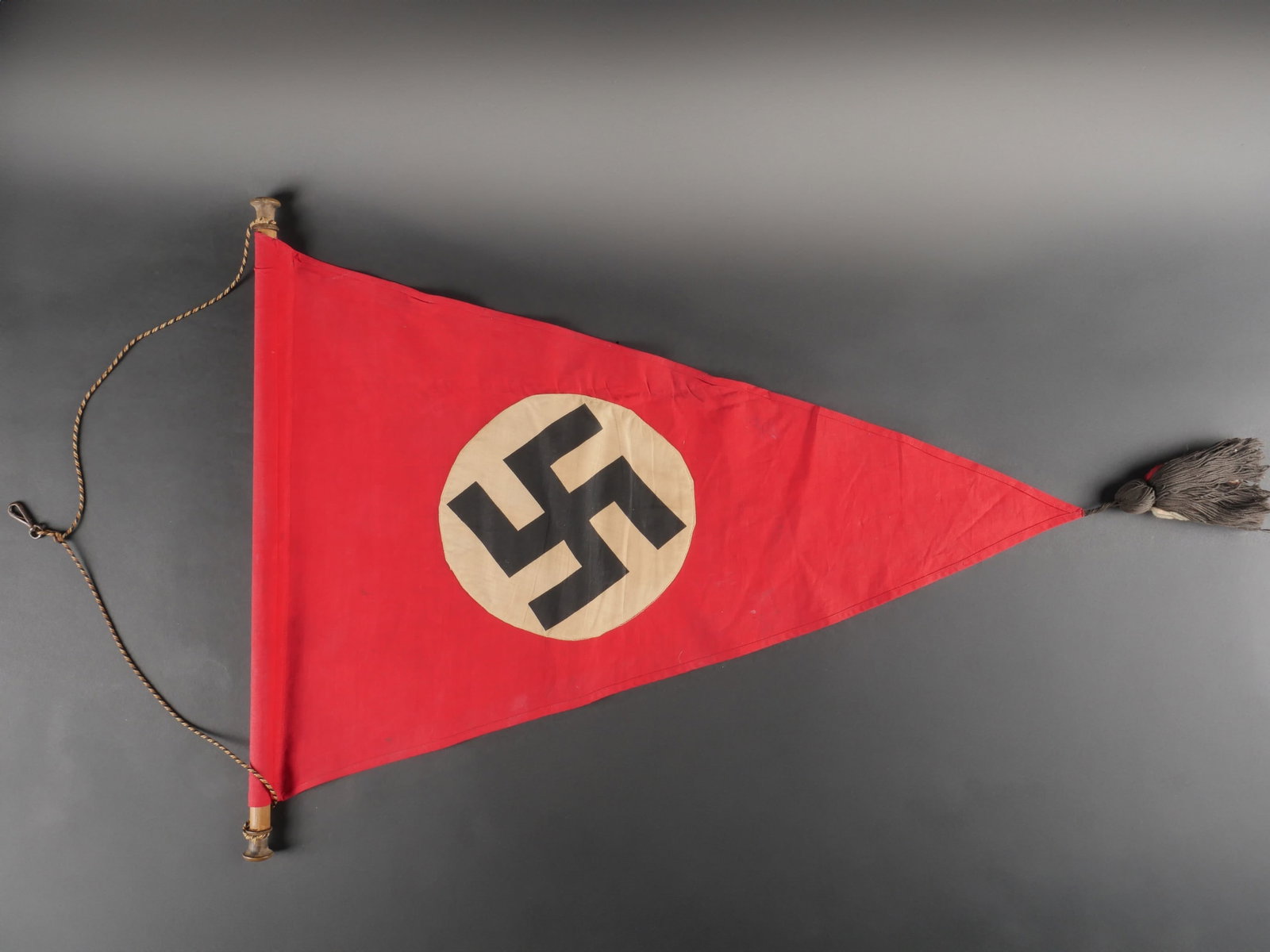 Drapeau allemand. German flag.: Drapeau allemand. En tissu coton rouge. Mat en bois complet. Systeme d attache au mur, realise par un tressage de fil rouge/blanc/noir. Biface. Format triangulaire. Insigne national allemand imprime e