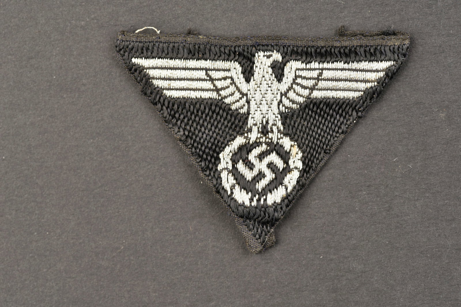 Aigle de calot du Teno. Teno cap eagle.: Aigle de calot du Teno. Modele tisse en fils argent sur fond noir. Insigne triangulaire. Les bordures sont pliees d origine. A noter une certaine usure et patine de la piece. Etat II+. Teno cap eagle.