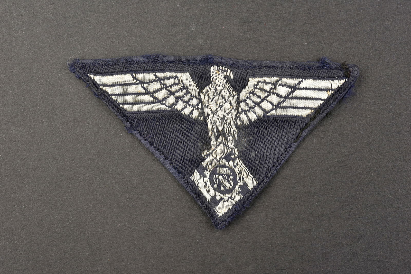 Insigne de coiffure TENO. Teno cap badges.: Insigne de coiffure Teno. Aigle tisse en fils argent sur fond noir. Modele triangulaire. Fabrication Ges Gesch G&W. Traces de colle au dos. A noter une certaine usure et patine de la piece. Etat II+.